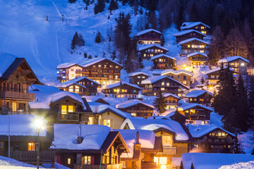 Wooden chalets covered with deep snow in cold winter season at the blue hours in Alps mountain region