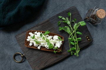 Obraz na płótnie Canvas Sandwich with creamy vegetarian cheese and micro greens, on an old wooden kitchen board and bottle of spices. The concept of fast healthy food, superfood
