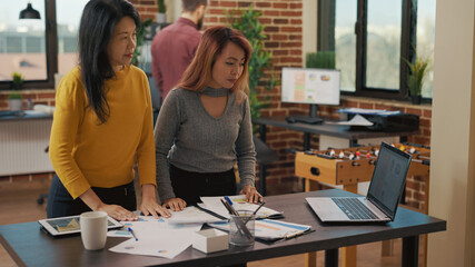 Coworkers doing teamwork on investment project, using information on laptop and financial charts on documents. Company employees working on marketing strategy for development.