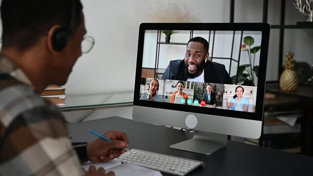 Distant learning, online education. View over a guy's shoulder, a computer screen with multiracial people, female teacher conducts online lecture for students by video call, virtual meeting concept