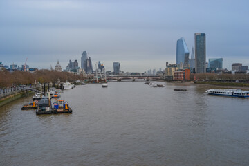 Naklejka premium UK, London, 11.12.2021:&nbsp;A view of the Thames with ships, tall buildings in the background and a cloudy sky.