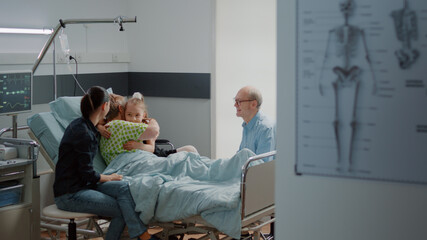 Child hugging sick patient in hospital ward bed at family visit with mother. Niece visiting retired woman at intensive care, having conversation to help with healthcare recovery.