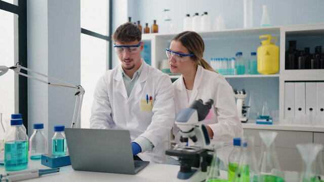 Young couple wearing scientist uniform using laptop at laboratory