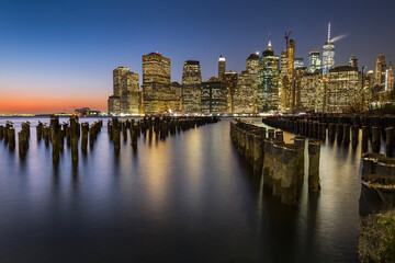 Fototapeta na wymiar View of lower Manhattan at dusk seen from Brooklyn. Remaining of an old pier can be seen at the foreground and city skyline in the background