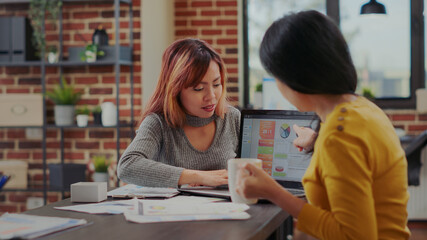 Team of asian women analyzing business charts on laptop and papers in office. Coworkers planning development strategy with financial statistics at briefing meeting. Sales research