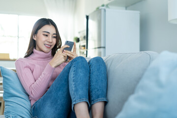 Asian beautiful woman sit on sofa and chat on mobile phone in house.