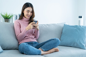 Obraz premium Asian beautiful woman sit on sofa and chat on mobile phone in house.