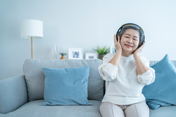 Asian senior mature woman enjoy listening to music and dancing on sofa