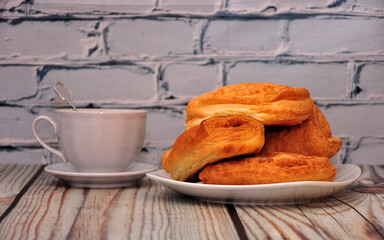 A pile of fresh puff buns and a cup of black tea on a wooden table.