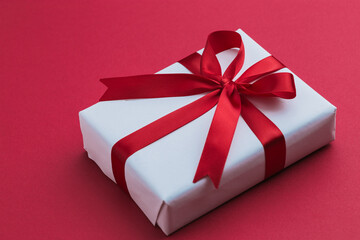 A small white gift with a red ribbon laying on a red background