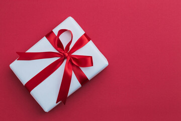A small white gift with a red ribbon laying on a red background