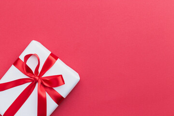 A small white gift with a red ribbon laying on a red background