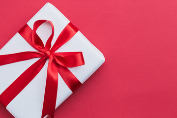 A small white gift with a red ribbon laying on a red background