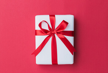 A small white gift with a red ribbon laying on a red background