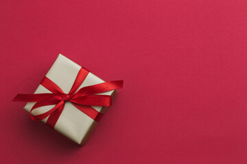 A small gold gift with a red ribbon laying on a red background