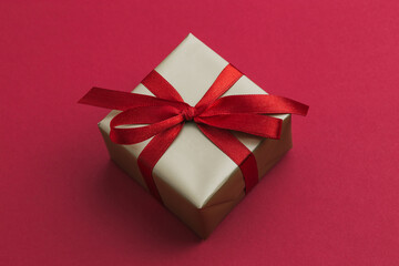 A small gold gift with a red ribbon laying on a red background