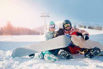 Happy young lover couple man and woman snowboarders on background of ski resort, sun light