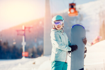 Portrait young woman snowboarder stands with snowboard sunlight, winter ski lift resort
