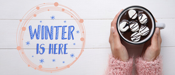 Female hands holding cup of tasty hot chocolate with marshmallow on white wooden background. Hello...