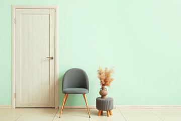 Modern chair and pouf with vase near green wall