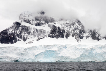 Landscape of huge icebergs and hills in the sea on a foggy day in Antarctica