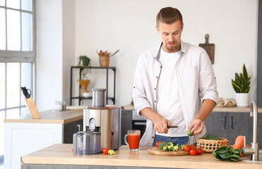 Young man preparing healthy vegetable juice in kitchen