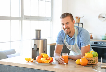 Young man with glass of fresh fruit juice near modern juicer in kitchen