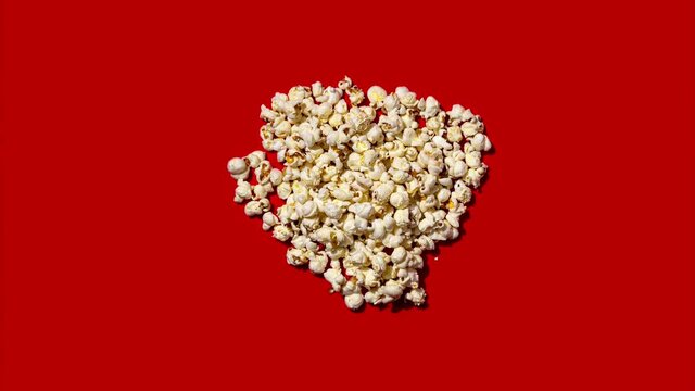 Stop motion animation with popping popcorn seed in a Heart shape on a red background. Love the cinema, dating, and Valentine's Day concept 