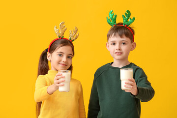 Funny little children with reindeer horns and milk on color background