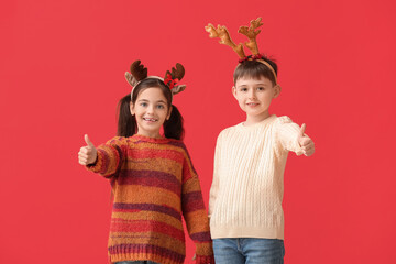 Funny little children with reindeer horns showing thumb-up on color background