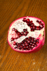 Half of a huge pomegranate fruit with bright red grains on a wooden background.