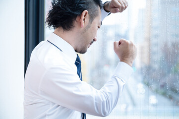 何かに憤って窓を叩くアジア系のビジネスマン男性のアップ　エクゼクティブ求人などに　コピースペースあり