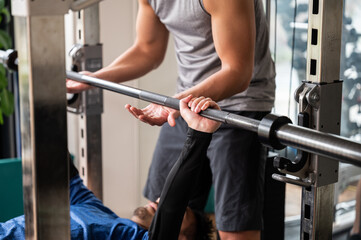 A trainer who teaches strength training and a person who takes private lessons with a barbell. No face.