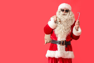 Santa Claus in sunglasses with candy cane and sack bag on red background