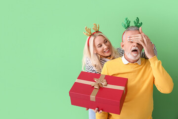 Happy mature woman greeting her husband on Christmas eve against color background