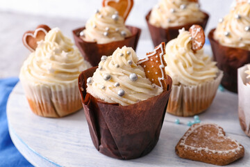 Wooden board with delicious Christmas cupcakes on table
