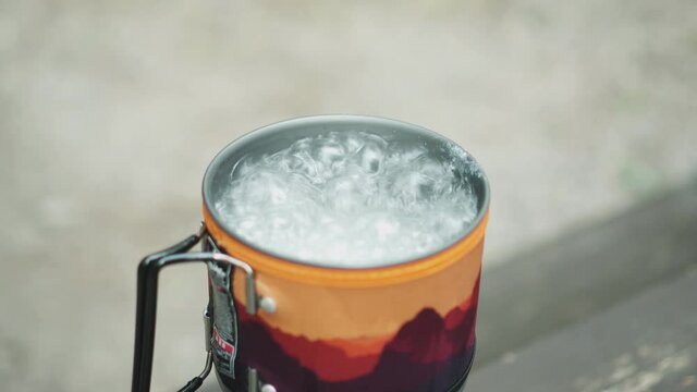 Close up shot of a man picking spoon from a boiling water in an enamel red and yellow tourist mug. 