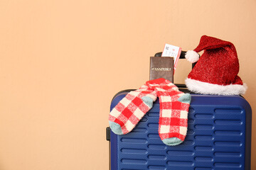 Fototapeta na wymiar Suitcase with Santa hat, socks and documents near color wall, closeup. Christmas vacation concept