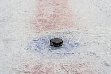 Black old puck lies in center of throw-in circle on skate-cut ice of hockey rink.
