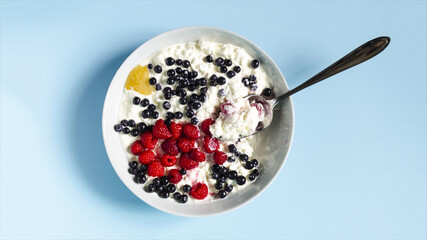 The concept of a healthy breakfast.  Berries and cottage cheese with sour cream in a light flatley plate