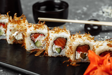 sushi rolls with cream cheese, fried salmon, tuna shavings or dried bonito, cucumber, nori. Chopsticks holding fresh katsuobushi roll in Japanese restaurant closeup