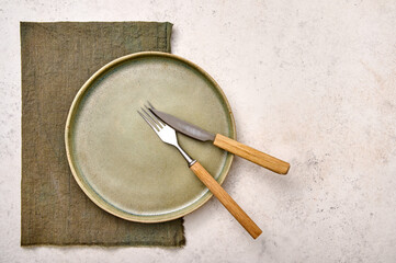 Set of empty green plate with napkin, fork and knife on white textured background. Design concept, copy space