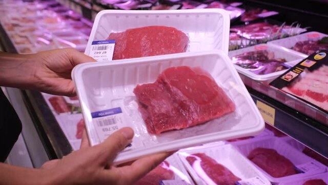 Human hands holding packaged fresh meat fillets, choosing beef for cooking in supermarket, butcher's shelves 