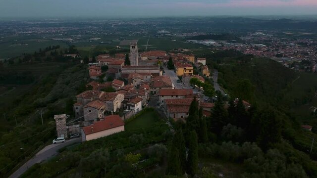 Old traditional Italian medieval castle village San Giorgio with a scenic church tower on a hill in Valpolicella, Verona, Italy in autumn by sunset at Lake Garda. Cinematic aerial drone flying