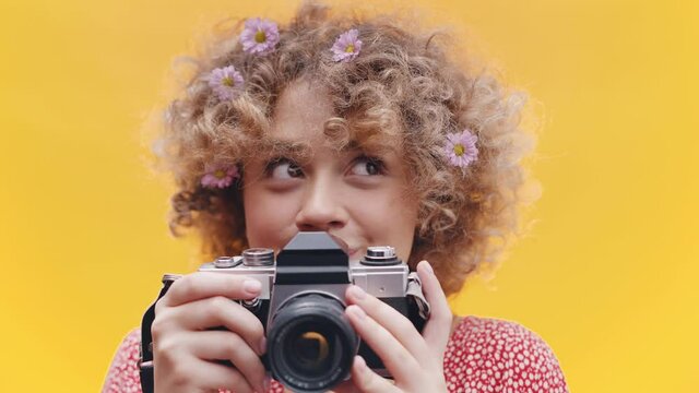 Blonde curly hair yong woman with flowers looks from side to side, is happy, holds the camera - Close Up