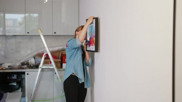 Smiling woman decorating apartment, Hanging picture on the wall - Medium Full Shot