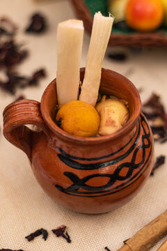 Jarrito tradicional mexicano de ponche de frutas navide&ntilde;o con ca&ntilde;a, tejocote y guayaba. Sobre la mesa, mantel de yute, canela y hojas de jamaica