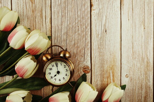 Vintage alarm clock with pink tulip flower bouquet on wooden background