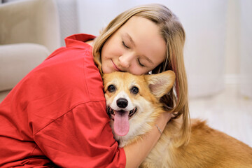 Cute little girl hugging corgi dog with love eyes closed, smiling. Dog lover with domestic animal. soft selective focus