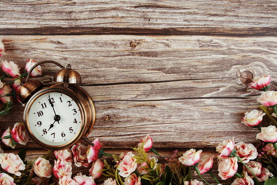 Alarm clock with Pink roses flowers border frame on wooden background